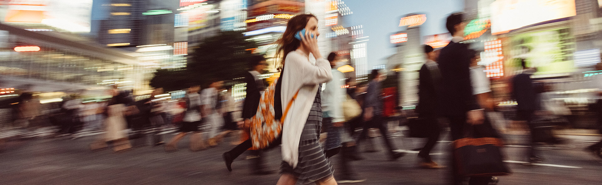 Frau am Telefon überquert mit vielen anderen Menschen die Straße einer Großstadt